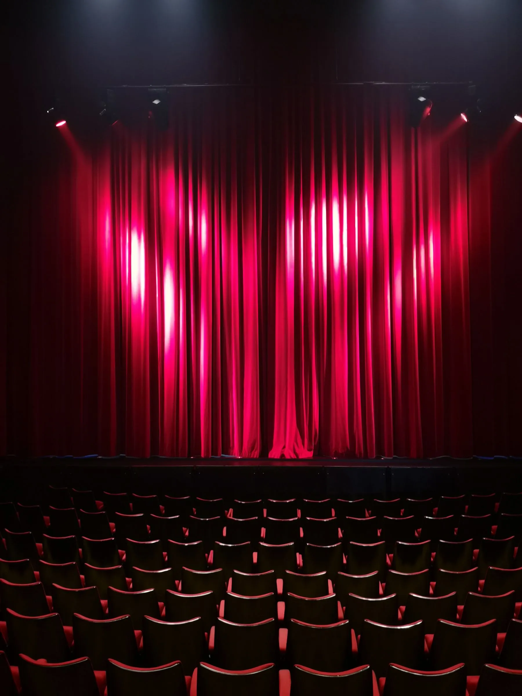A red stage curtain lit from above in an empty theatre